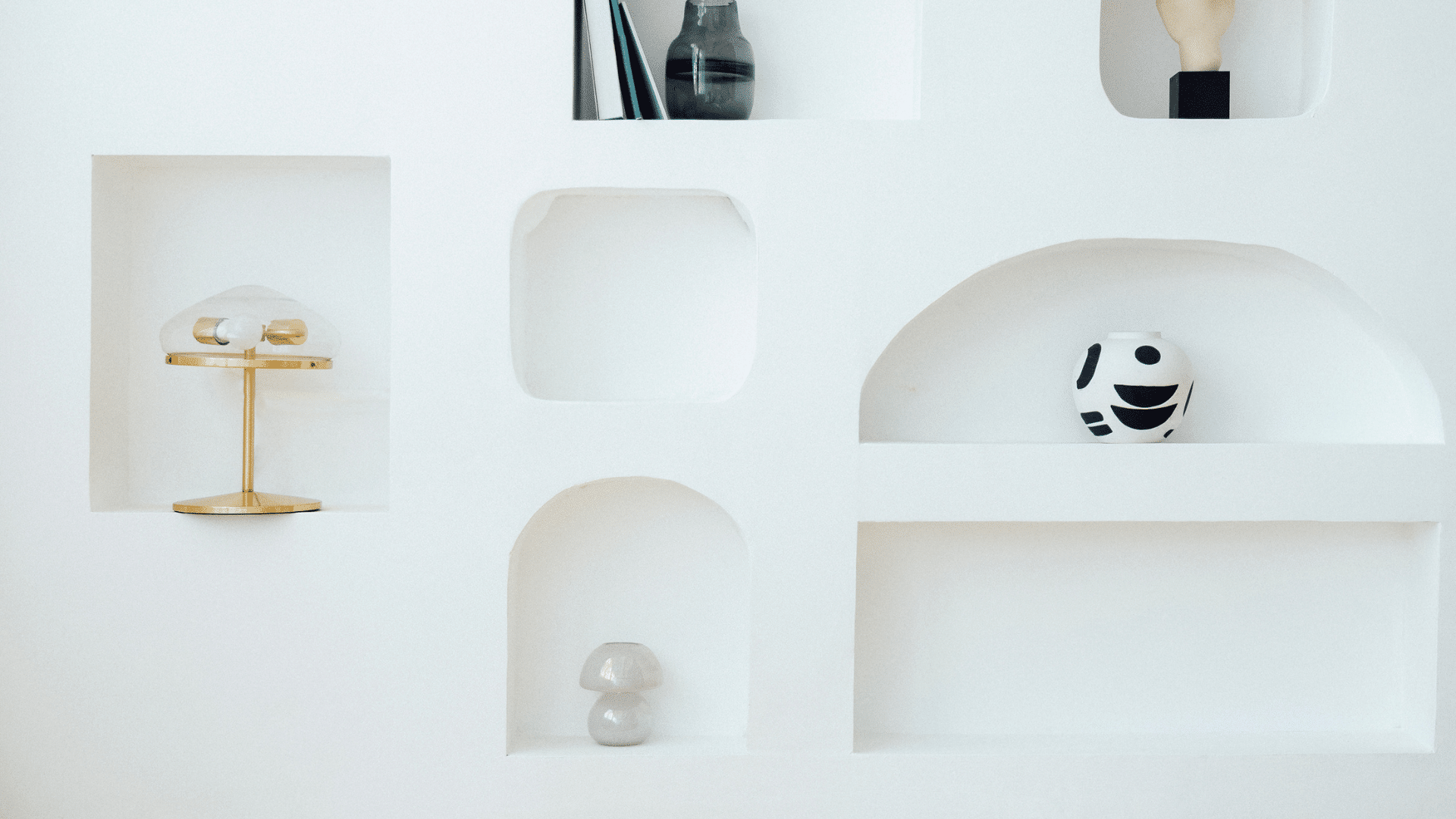 Mur blanc minimaliste à Var avec étagères intégrées, vase noir et blanc, petites lampes, objets déco.