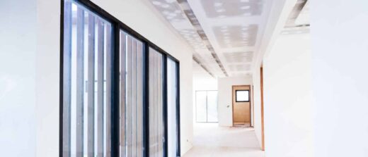 Un couloir lumineux avec portes vitrées, plafond inachevé et porte en bois au fond. Ambiance accueillante.